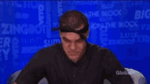 a man in a black shirt is sitting in front of a blue wall with a globe logo on it