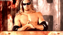 a shirtless wrestling wrestler wearing sunglasses is sitting at a table .