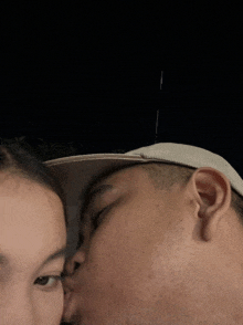 a man and a woman kissing with the man wearing a hat