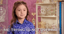 a little girl in a blue shirt is standing in front of a shelf with crowns on it .