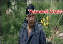 a man in a blue jacket is standing in front of trees and flowers with the words thirudan chat written above him
