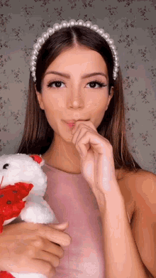 a woman wearing a headband with pearls is holding a teddy bear