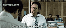 a man in a white shirt and tie is talking to another man in an office while smoking a cigarette .