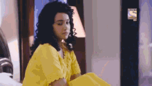 a woman in a yellow dress sits on a bed in front of a sign that says sony television