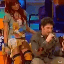 a man is singing into a microphone while a woman sits next to him ..