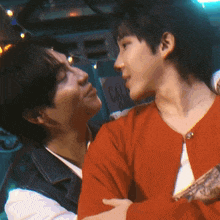 a man in a red sweater is hugging another man in front of a sign that says call
