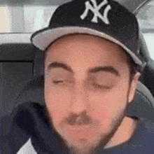 a man with a beard wearing a ny yankees hat is sitting in the back seat of a car .