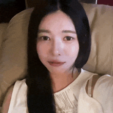 a woman with long black hair is sitting on a couch and taking a selfie