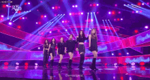 a group of women are dancing on a stage with purple lights