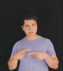 a young man in a purple shirt is pointing at his chest