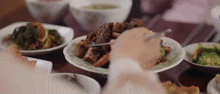 a person is eating a plate of food with a knife and fork at a table .