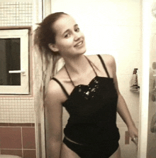 a woman in a black tank top and black underwear is smiling in a bathroom