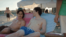 a man in a green shirt stands next to two men on a beach