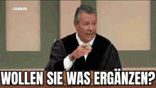 a man in a judge 's robe is sitting in front of a microphone and says wollen sie was erganzen .