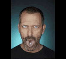 a man with a beard is sticking out his tongue and holding a pill in his mouth .