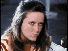 a woman with long hair and a striped shirt is looking at the camera .