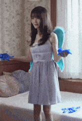 a woman in a blue dress is standing on a bed holding blue wings