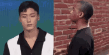 a man with a shaved head is standing in front of a brick wall and talking to another man .