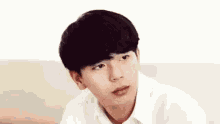 a young man with black hair and a white shirt is sitting on a couch looking at the camera .