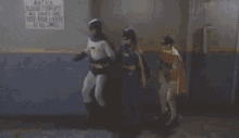 a batman and batgirl are standing next to each other in front of a sign that says keep door locked at all times .