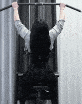 a woman is sitting on a bench with her back to the camera holding a bar over her head
