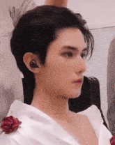 a close up of a young man wearing a white shirt with a red rose on his shoulder .