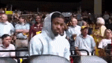a man wearing a hoodie is sitting in a crowd of people watching a game