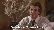 a man in a white shirt and tie says " no more screw ups " in front of a vase of flowers