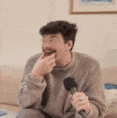a man with glasses and a mustache is sitting on a couch holding a microphone and eating something .