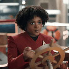 a woman in a red jacket is holding a wooden ship 's steering wheel .