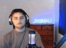 a man wearing headphones is sitting in front of a microphone with a sign that says jxonau in the background