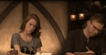 a man and a woman are sitting at a table writing on paper .