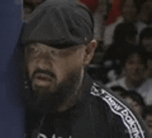 a man with a beard wearing a hat and a black jacket is standing in front of a crowd .