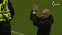 a man applauds on a soccer field with a police officer behind him