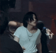 a young man with long hair is wearing a white t-shirt and a chain around his neck .