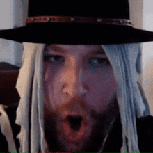 a man with a beard wearing a hat and a wig with his mouth open
