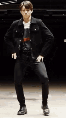 a young man in a black jacket and black pants is standing on one leg .