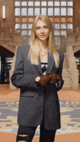 a woman wearing a grey jacket and brown gloves stands in front of a staircase