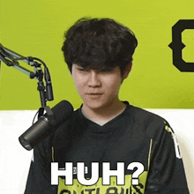 a young man is sitting in front of a microphone with the words huh written on his shirt .