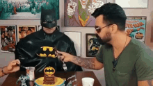 a man in a batman costume is cutting a cake