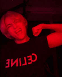a man wearing a black shirt with the word celine on it is dancing in a dark room with red lights .