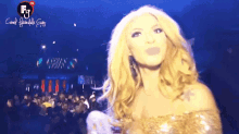 a woman in a gold dress stands in front of a crowd with a fg logo on the bottom