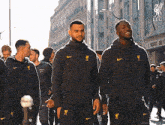 a group of men are walking down a street and one of them is wearing a nike jacket