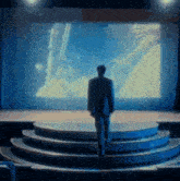 a man in a suit stands on a stage in front of a screen that says ' s miller ' on it