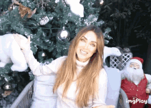 a woman sitting in front of a christmas tree with a gif play watermark