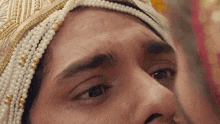 a close up of a man 's face with a pearl headpiece on