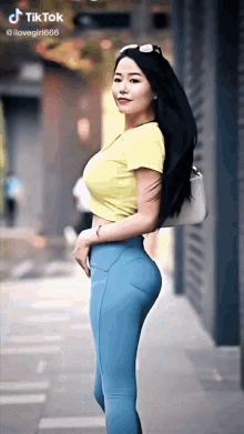 a woman wearing a yellow crop top and blue leggings is standing on a street .