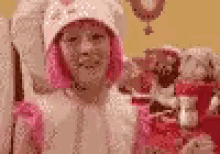 a little girl with pink hair and a white hat is standing in a room with a clock in the background .