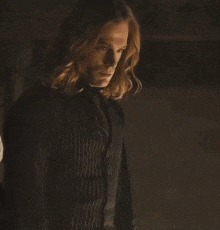 a man with long hair is standing in a dark room with a blurred background .