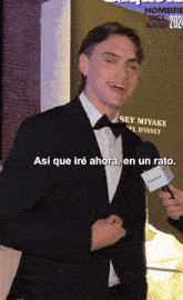a man in a suit and bow tie is talking into a microphone and says así que